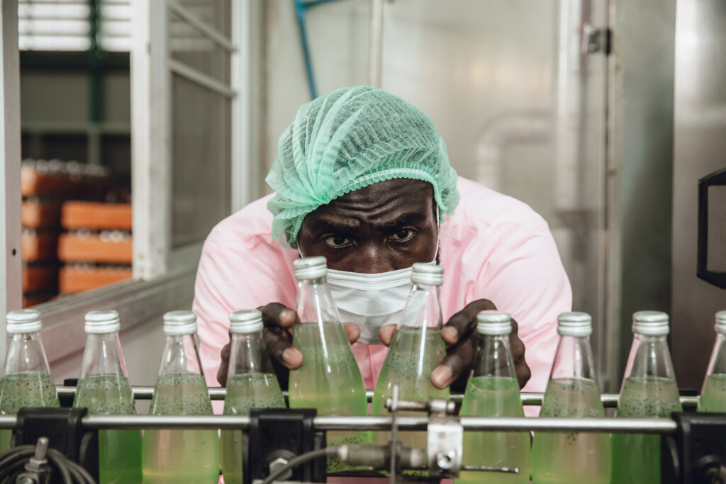 African Nigerian staff worker work in drink factory quality check at conveyor belt product line