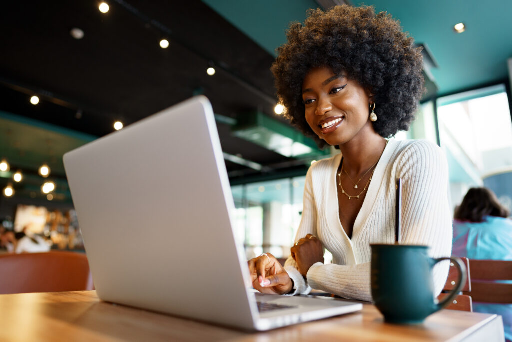 Smiling young african woman sitting with laptop in cafe